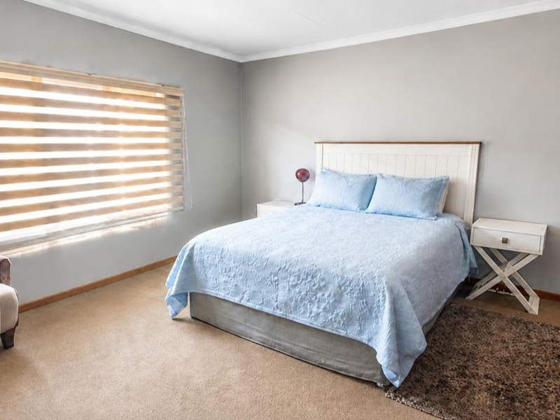 A well-maintained bedroom featuring neutral wall tones, carpeted flooring, a built-in wardrobe, and modern zebra blinds for adjustable natural light.