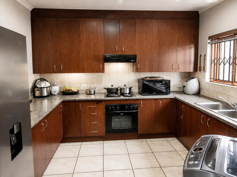 A functional kitchen featuring dark wood cabinetry, granite countertops, a built-in oven with hob, and tiled flooring with a window featuring security bars.