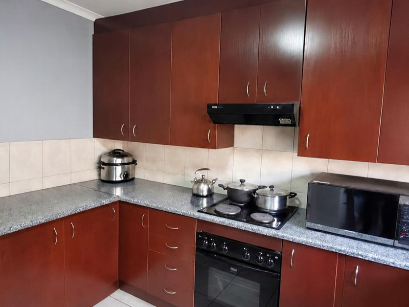 A functional kitchen featuring dark wood-look cabinetry, granite countertops, a tiled backsplash, and integrated cooking appliances including an oven and electric hob.