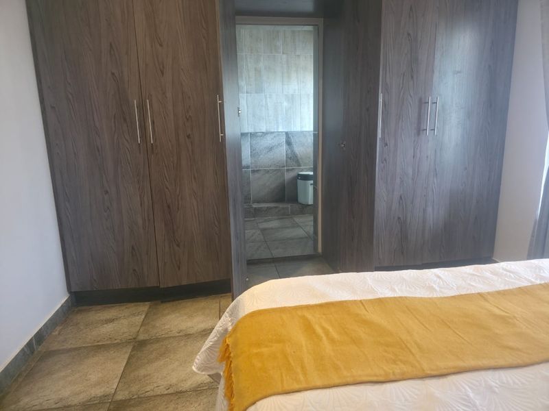 Bedroom featuring dark wood-grain built-in cupboards, tiled flooring, and direct access to an en-suite bathroom.