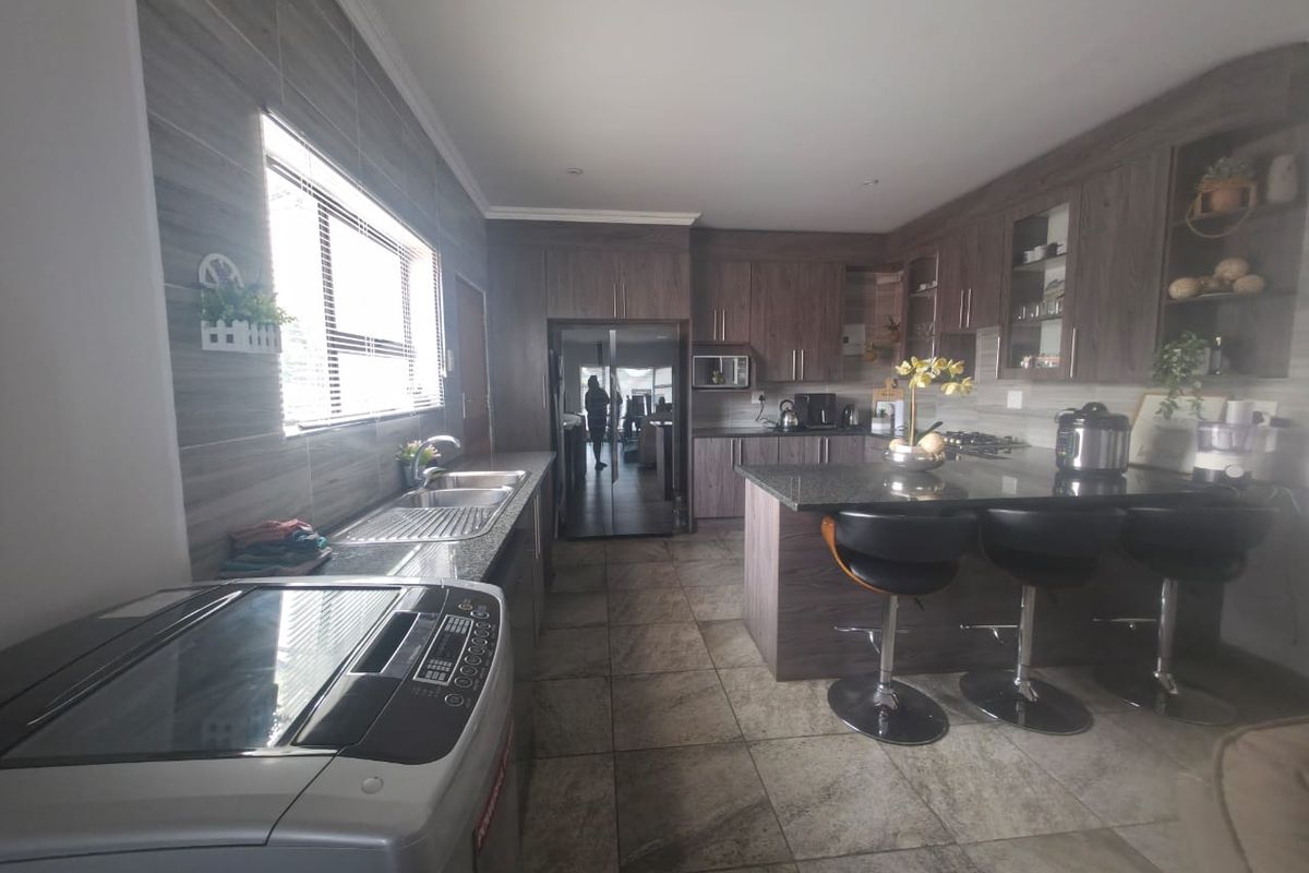 Modern kitchen featuring dark wood cabinetry, granite countertops, a central island with breakfast bar seating, and tiled flooring throughout.