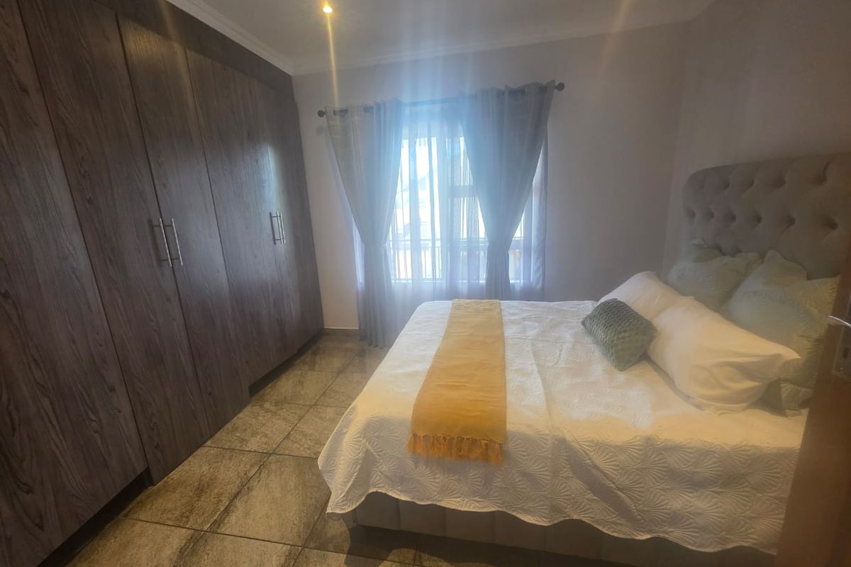 A well-maintained bedroom featuring dark wood built-in cupboards, tiled flooring, and natural light through a window with curtain rails.