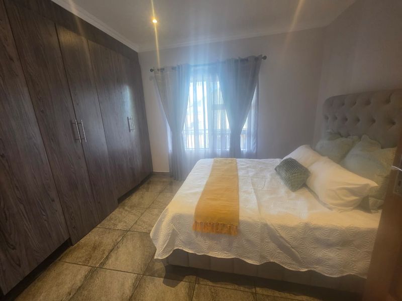 A well-maintained bedroom featuring dark wood built-in cupboards, tiled flooring, and natural light through a window with curtain rails.