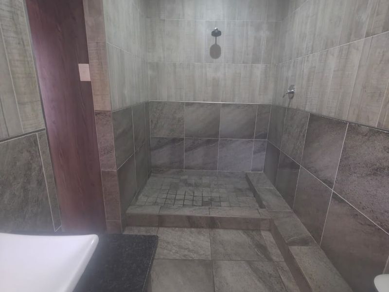 Modern bathroom featuring a spacious walk-in shower with grey tiled finishes and a vanity basin with a granite countertop.