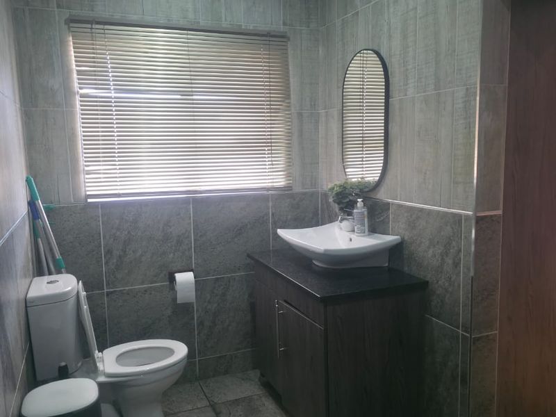 A modern bathroom featuring grey tiled walls and flooring, a dark wood vanity cabinet with a vessel sink, and a window with venetian blinds.