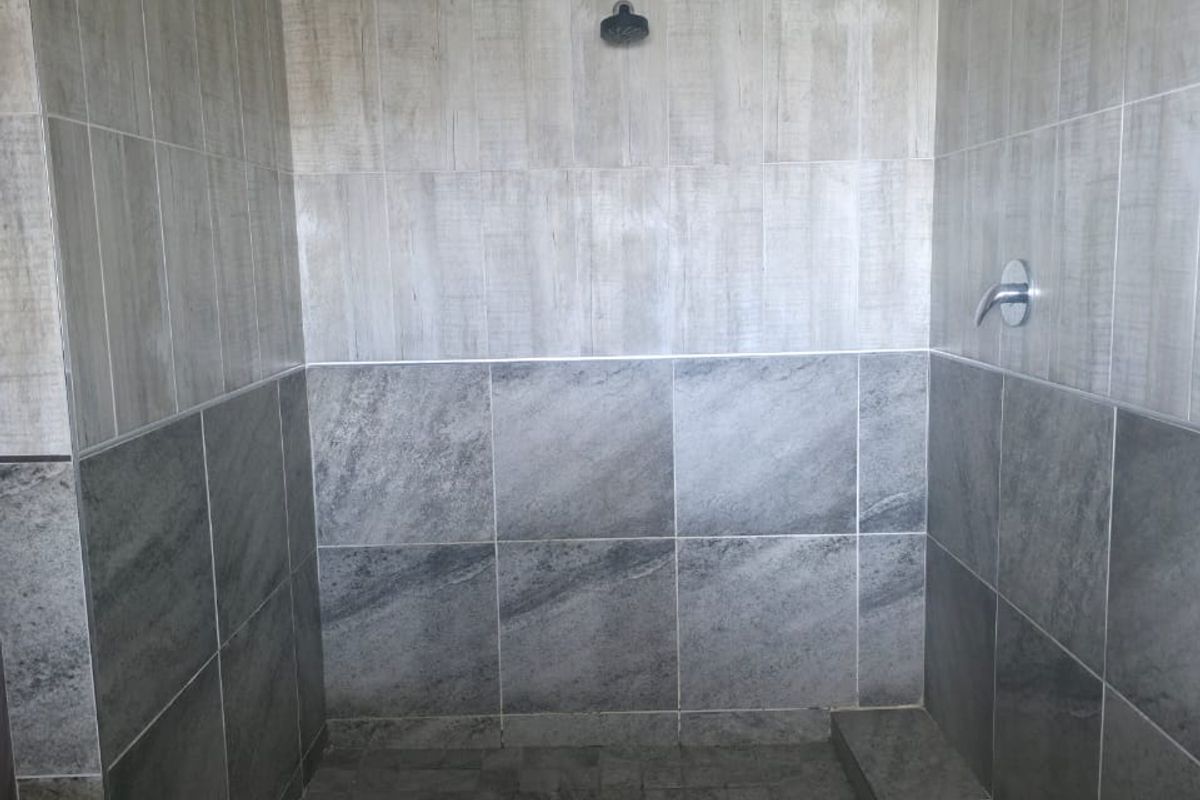 A modern walk-in shower featuring dual-tone grey tiling, a fixed shower head, and a chrome mixer tap.