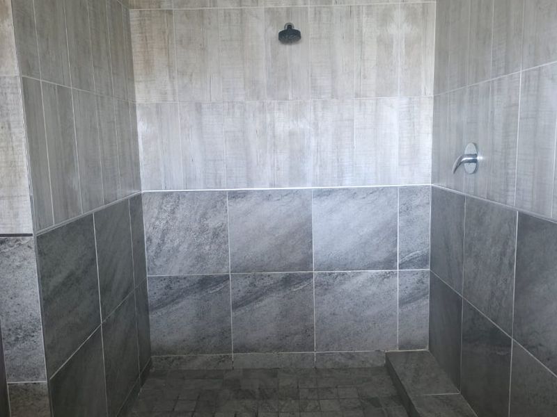 A modern walk-in shower featuring dual-tone grey tiling, a fixed shower head, and a chrome mixer tap.