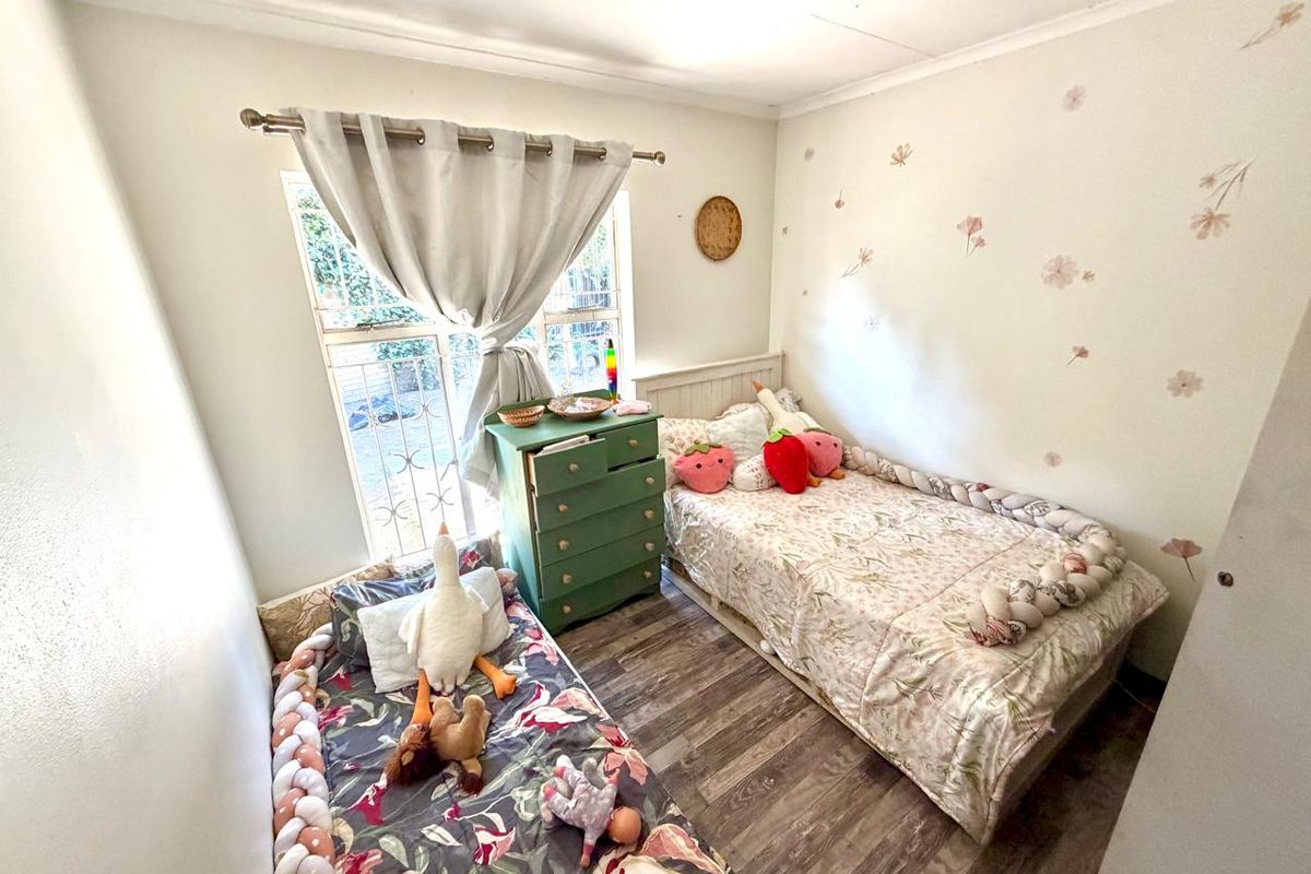 A cozy bedroom featuring laminate flooring, a window with security bars, and neutral wall finishes.