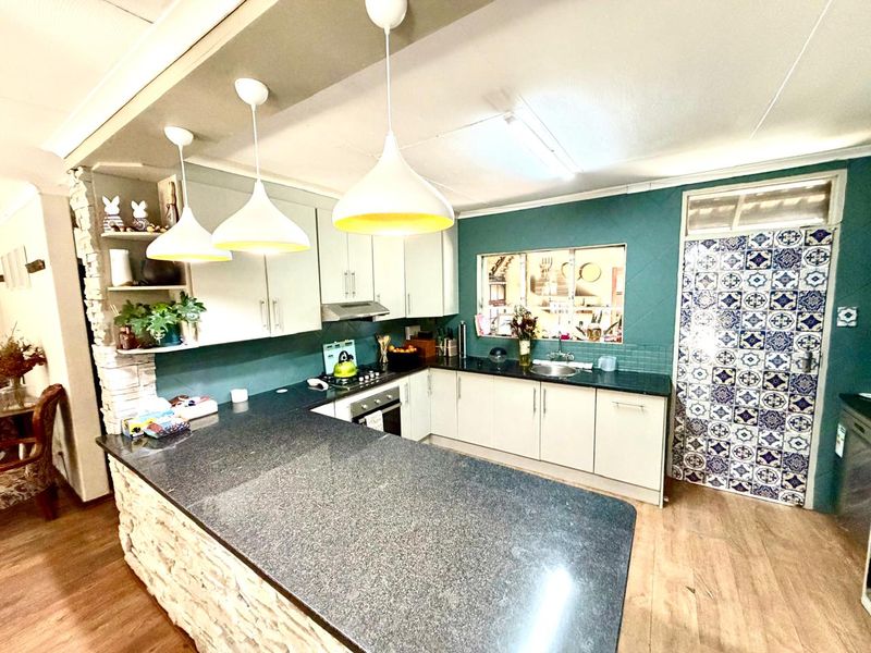 A functional kitchen featuring granite countertops, a stone-clad breakfast bar, built-in appliances, and a distinctive decorative tile feature wall.