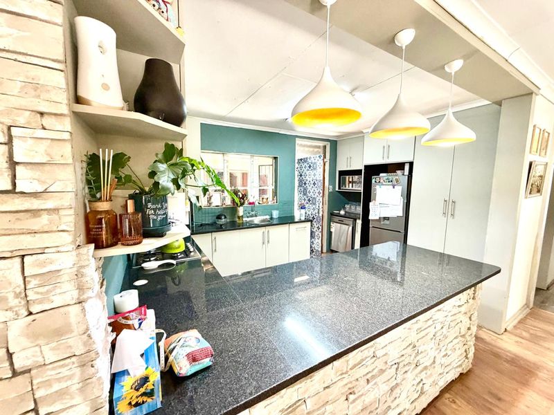 A functional kitchen featuring a stone-clad breakfast bar, granite countertops, ample cabinetry, and modern pendant lighting, creating a warm and inviting culinary space.