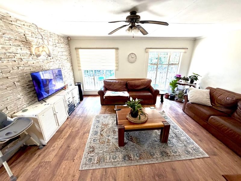 Spacious living room featuring a stone accent wall, laminate flooring, and a ceiling fan, with large windows fitted with security bars.