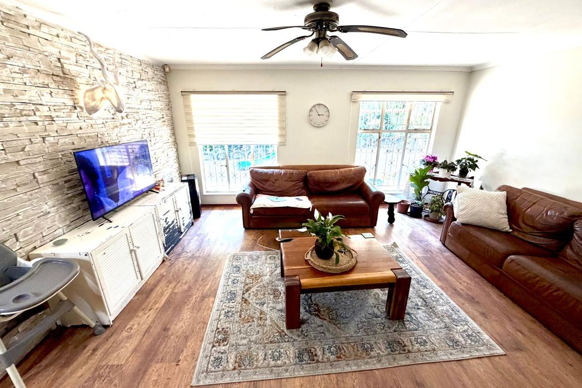 Spacious living room featuring a stone accent wall, laminate flooring, and a ceiling fan, with large windows fitted with security bars.