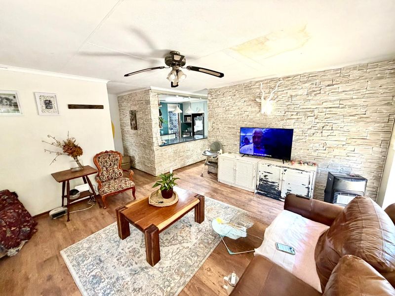 Open plan living area featuring a stone veneer accent wall, ceiling fan, and laminate flooring, with a visible water stain on the ceiling.