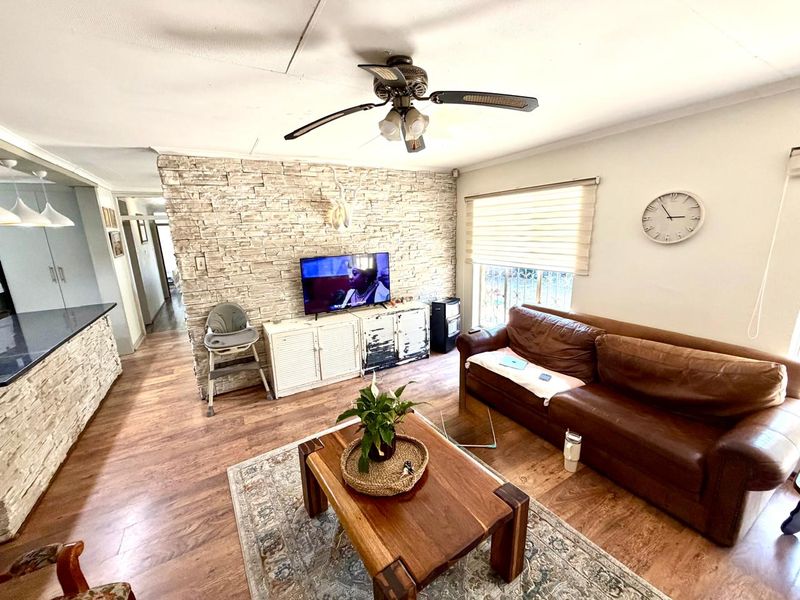 A living room featuring a stone veneer accent wall, laminate flooring, and a ceiling fan, with natural light provided by a window with roller blinds.