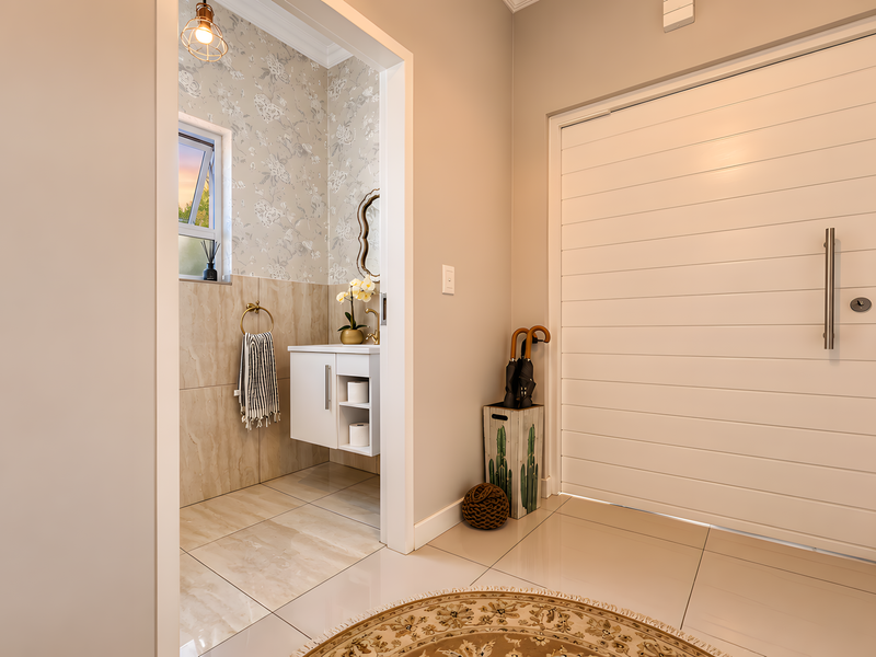 A bright and modern entrance hall featuring tiled flooring, a sleek horizontal panel front door, and an adjacent guest bathroom with elegant wall finishes.