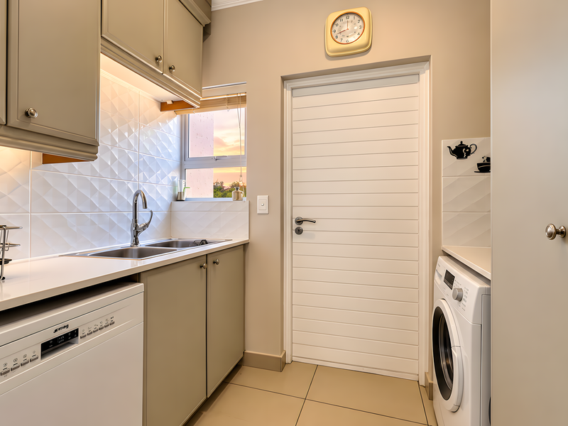 A well-appointed laundry room featuring modern built-in cabinetry, a stainless steel sink, tiled backsplash, and integrated appliance space.