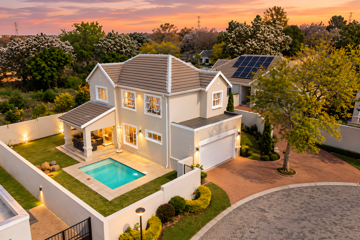 Aerial view of a well-maintained townhouse featuring a private swimming pool, covered patio, solar panels, and a paved driveway within a secure estate.
