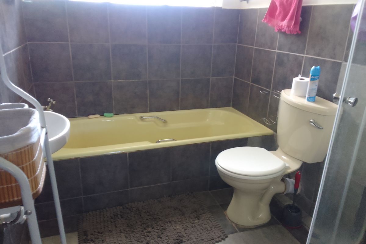 A functional bathroom featuring dark wall tiles, a built-in bathtub, and a standard toilet suite.