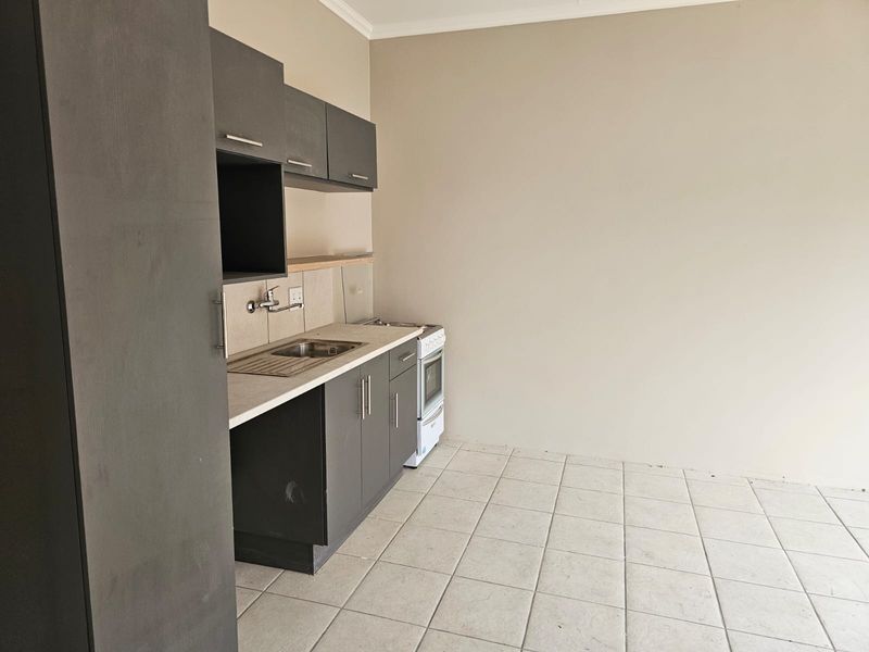 A compact, empty kitchen featuring dark grey cabinetry, a stainless steel sink, and a freestanding stove with tiled flooring.