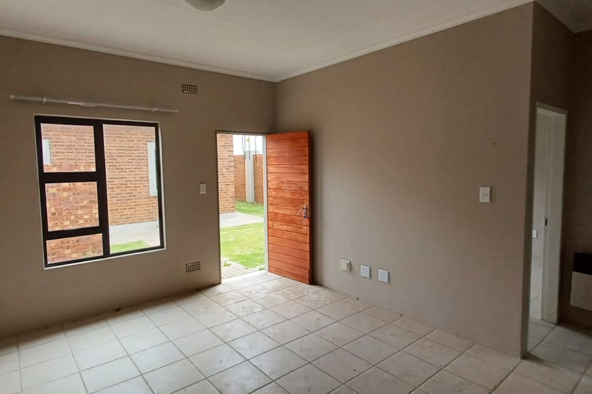 An empty living room featuring tiled flooring, a wall-mounted heater, and direct access to the exterior through a wooden door.