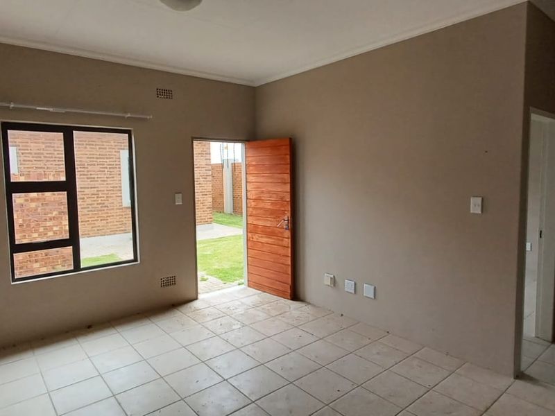 An empty living room featuring tiled flooring, a wall-mounted heater, and direct access to the exterior through a wooden door.