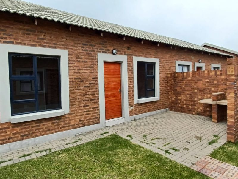 Rear exterior view of a face brick townhouse featuring a paved patio area with a built-in braai and a small private garden.