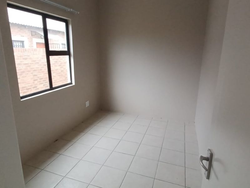 A compact, empty bedroom featuring neutral wall finishes, tiled flooring, and an aluminium-framed window providing natural light.