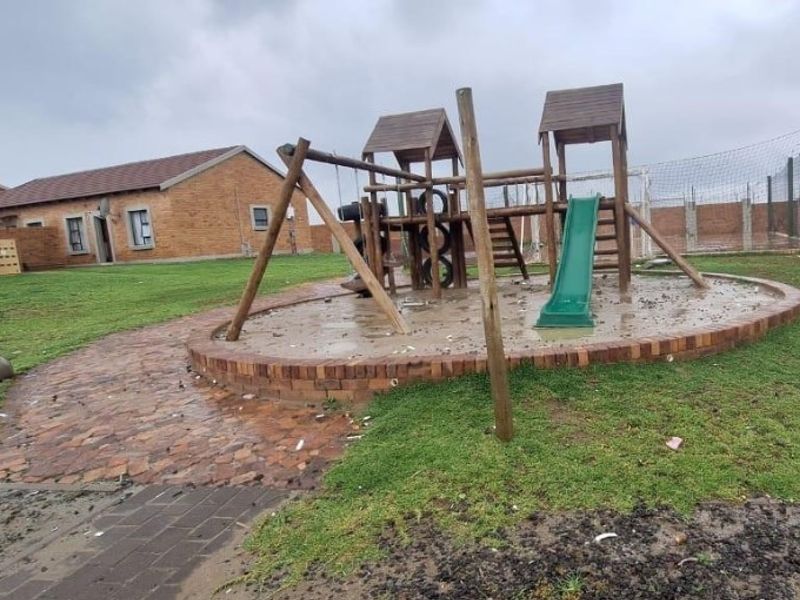 Communal outdoor area featuring a brick-paved pathway and a playground structure set within a landscaped garden space.