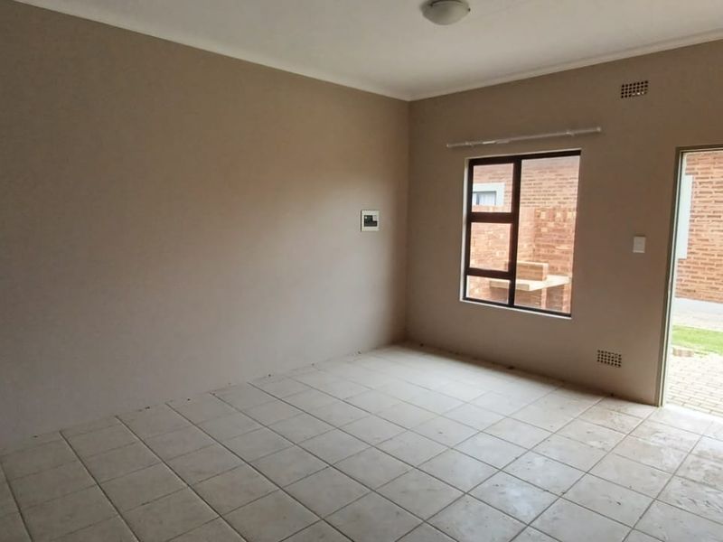 An empty, open-plan living area featuring tiled flooring, neutral wall tones, and direct access to an outdoor patio area.