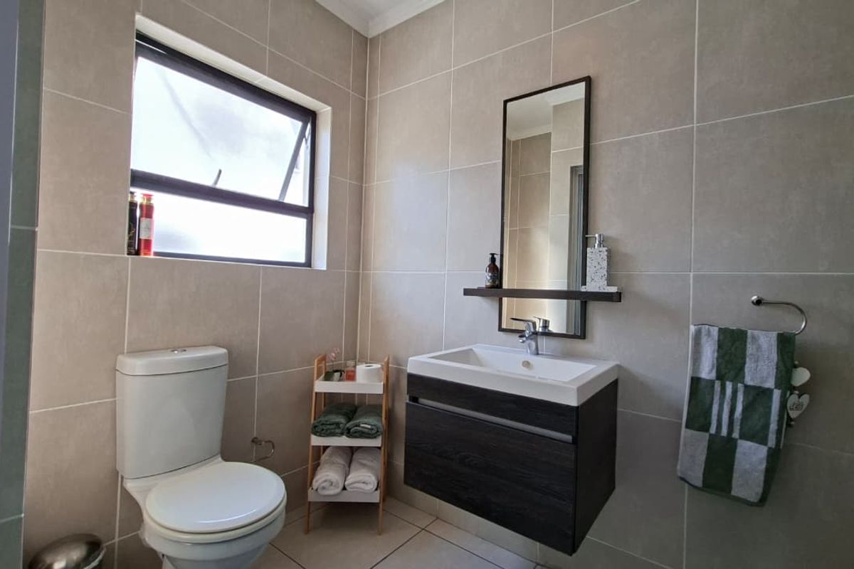 A modern, well-maintained bathroom featuring neutral wall tiles, a floating vanity with a basin, and a functional toilet.