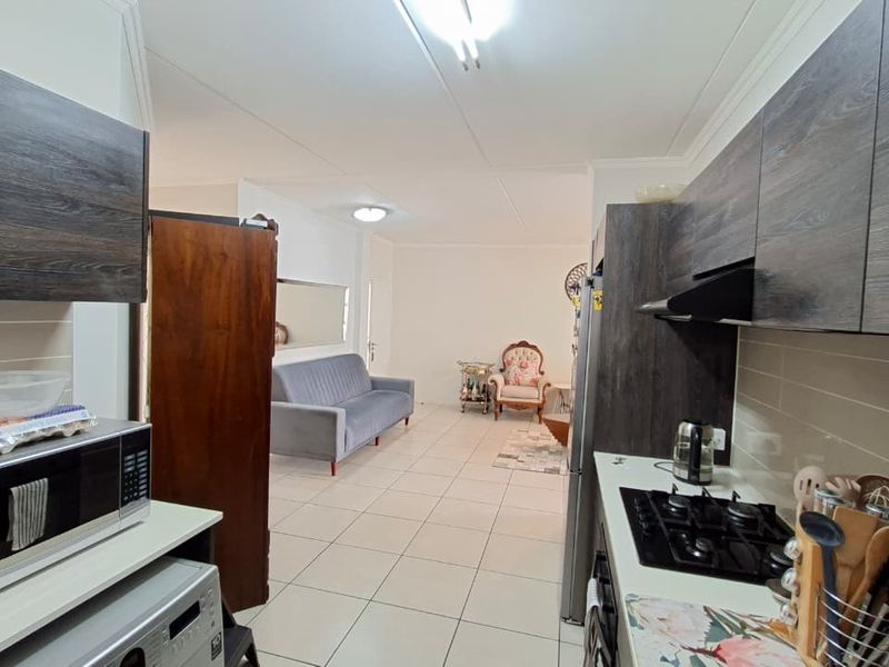 Open-plan kitchen and living area featuring modern dark wood cabinetry, gas hob, extractor fan, and neutral tiled flooring throughout.