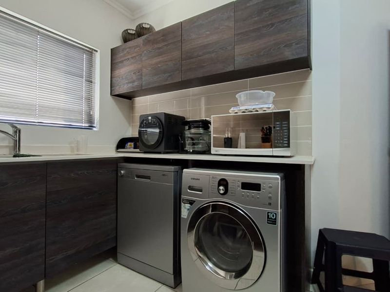 A functional laundry area featuring dark wood-finish cabinetry, a tiled backsplash, and integrated space for a washing machine and dishwasher.