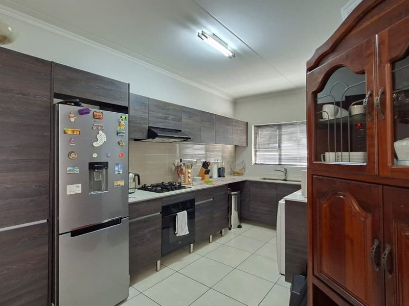 A functional kitchen featuring dark wood-look cabinetry, a gas hob, built-in oven, extractor fan, and tiled flooring with a neutral backsplash.