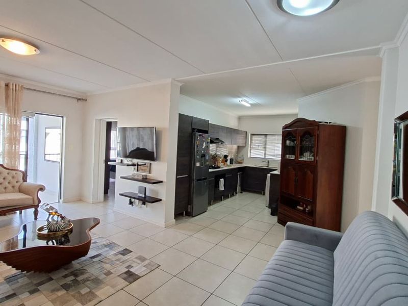 Spacious open-plan living area featuring tiled floors, a modern kitchen with built-in cabinetry, and direct access to a balcony through sliding glass doors.