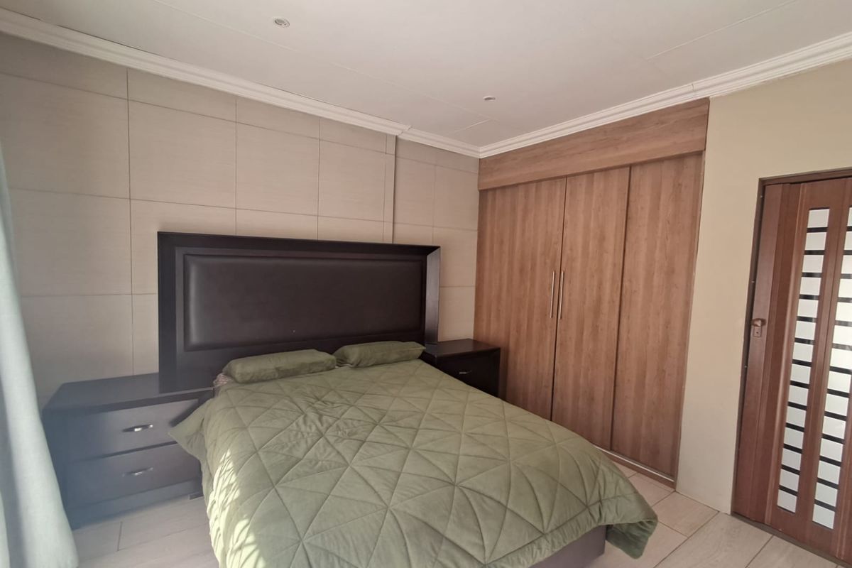 A well-maintained bedroom featuring built-in wooden cupboards, modern tiled flooring, recessed ceiling lights, and a decorative feature wall panel behind the bed.