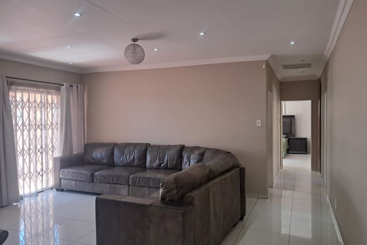 A spacious living room featuring polished porcelain floor tiles, recessed downlighting, and a secure sliding door with a metal security gate.