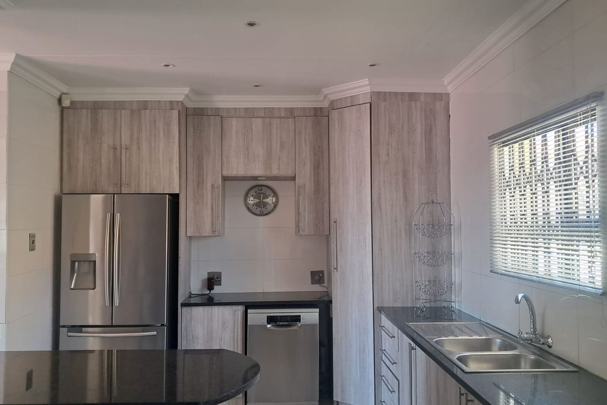 Modern kitchen featuring light wood-grain cabinetry, dark granite countertops, double basin sink, and integrated lighting, offering a clean and functional workspace.
