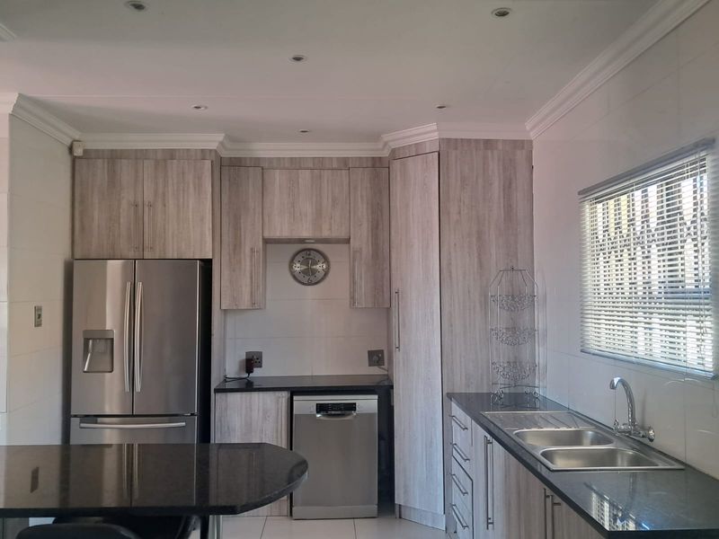 Modern kitchen featuring light wood-grain cabinetry, dark granite countertops, double basin sink, and integrated lighting, offering a clean and functional workspace.