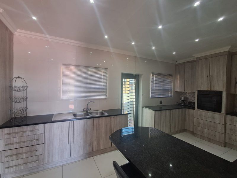 Modern kitchen featuring wood-grain cabinetry, granite countertops, double sink, built-in oven, and recessed lighting with tiled flooring throughout.