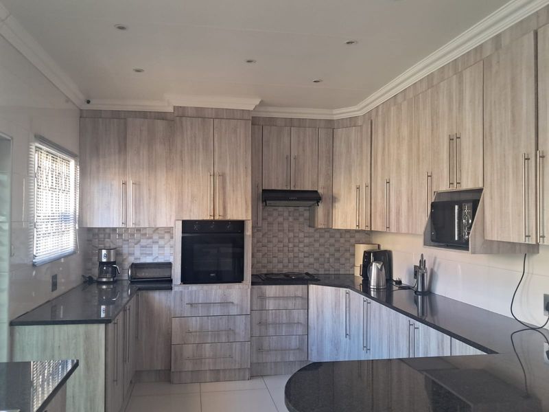 Modern kitchen featuring light wood-grain cabinetry, dark granite countertops, built-in oven, extractor fan, and a tiled backsplash with recessed lighting.