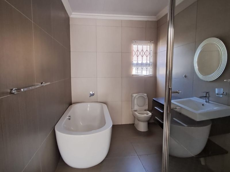 Modern bathroom featuring a freestanding bathtub, glass-enclosed shower, wall-mounted vanity with basin, and neutral floor-to-ceiling tiling.