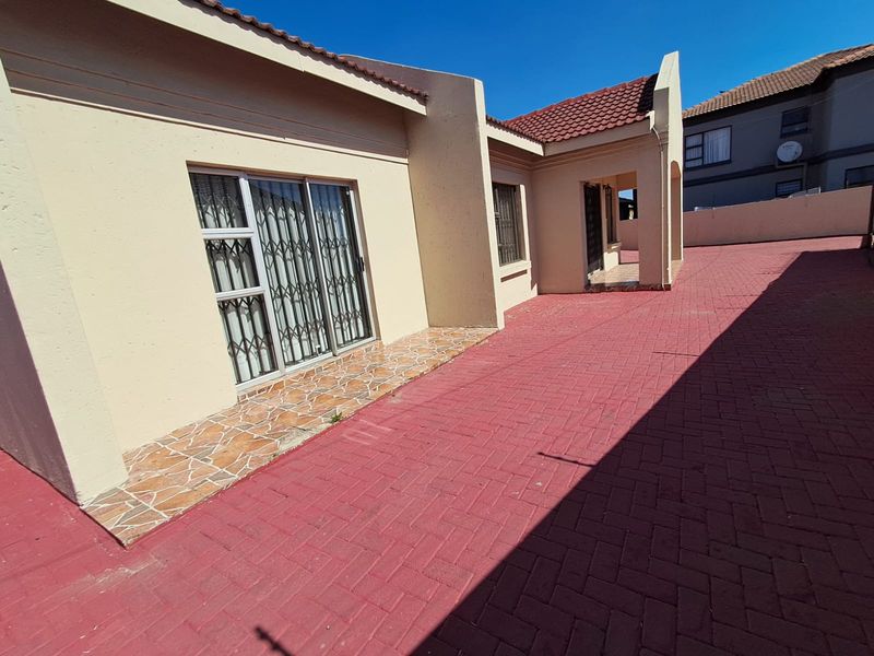 Rear exterior view of the property featuring a paved courtyard area, tiled patio, and sliding door access with security gates.