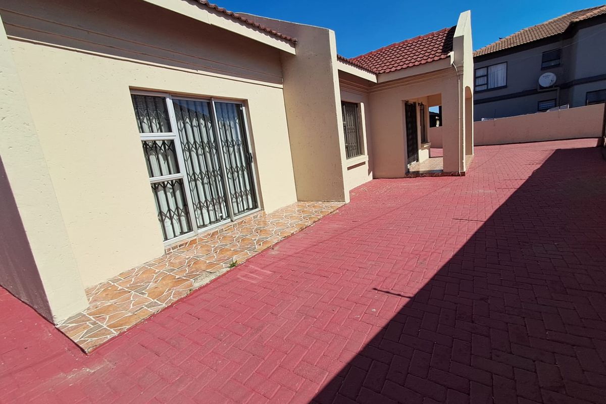 Rear exterior view of the property featuring a paved courtyard area, tiled patio, and sliding door access with security gates.