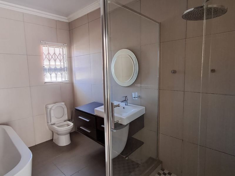 Modern bathroom featuring a freestanding bathtub, a glass-enclosed rainfall shower, and a sleek wall-mounted vanity with a ceramic basin.