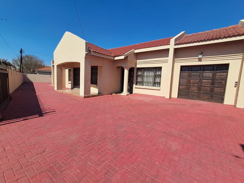 Front elevation of a single-story house featuring a large paved driveway, tiled roof, and an integrated garage with a security gate.