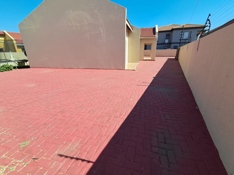 A spacious rear exterior area featuring red paved flooring, enclosed by high boundary walls with integrated electric fencing.
