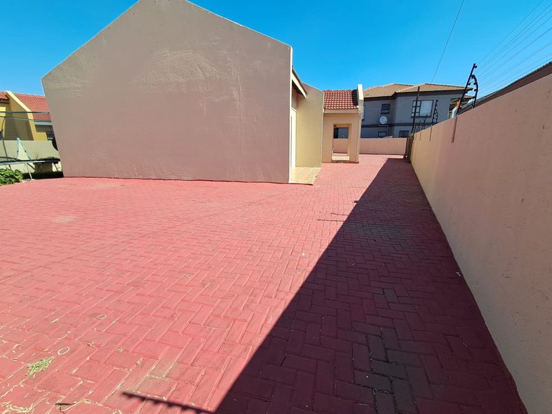 A spacious rear exterior area featuring extensive red brick paving, enclosed by high boundary walls with integrated electric fencing.