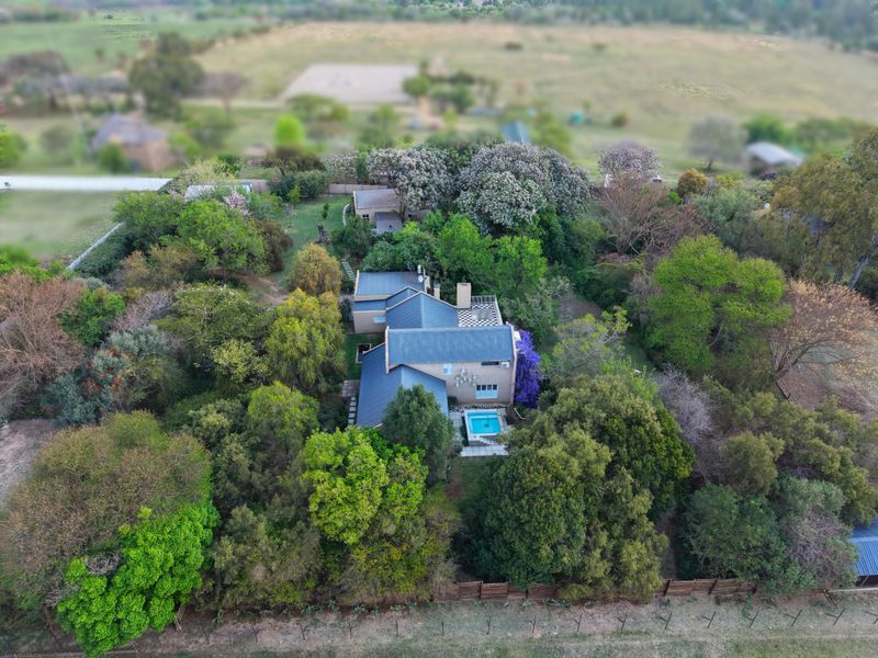 Aerial view of a residential property featuring a metal roof, a swimming pool, and extensive mature garden landscaping.