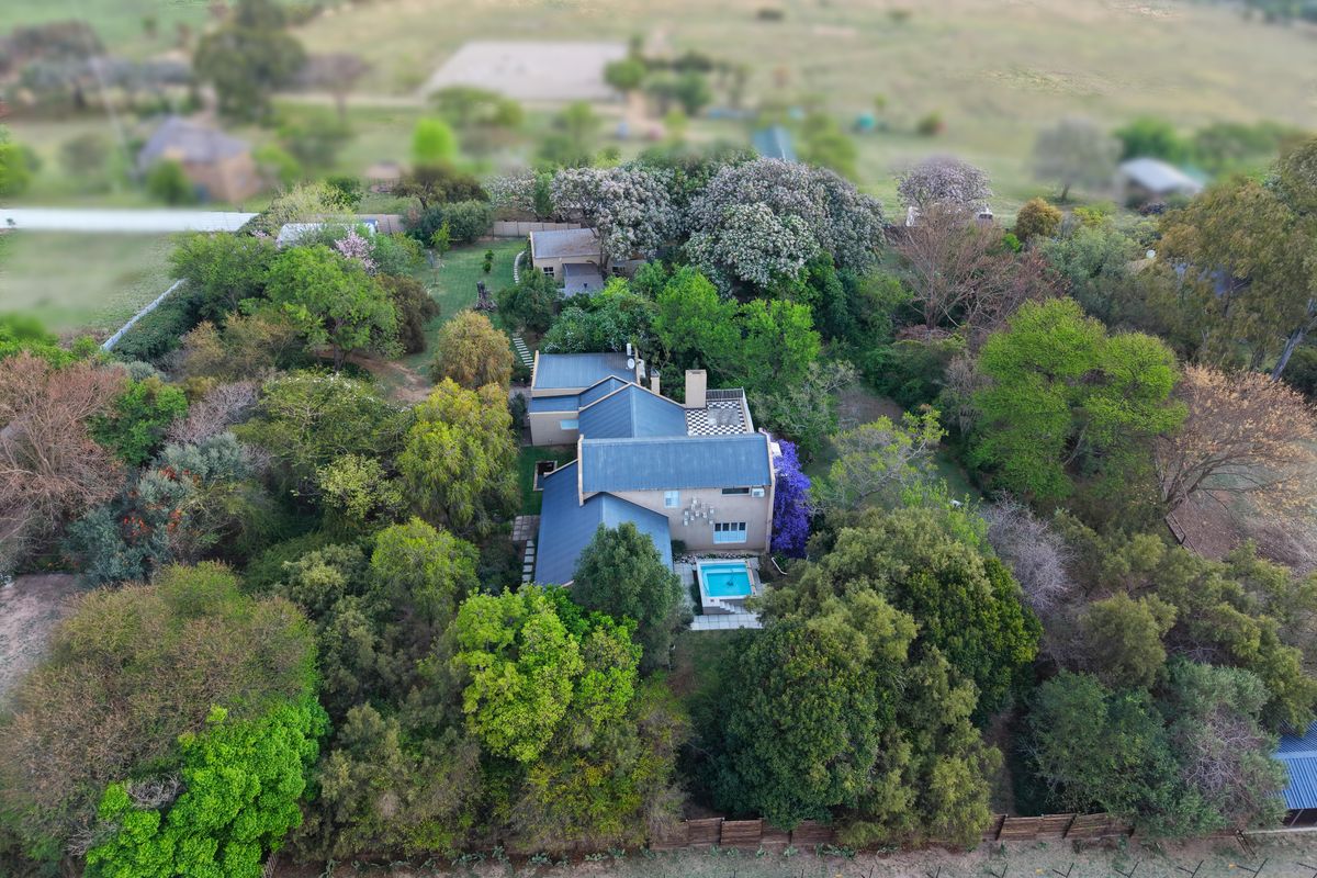 Aerial view of a residential property featuring a metal roof, a swimming pool, and extensive mature garden landscaping.