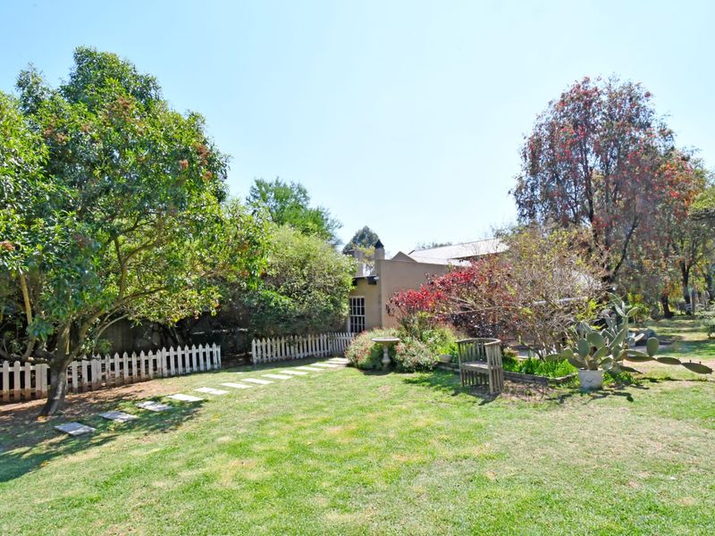 A well-maintained garden featuring a lush lawn, mature trees, a stone pathway, and a classic white picket fence.